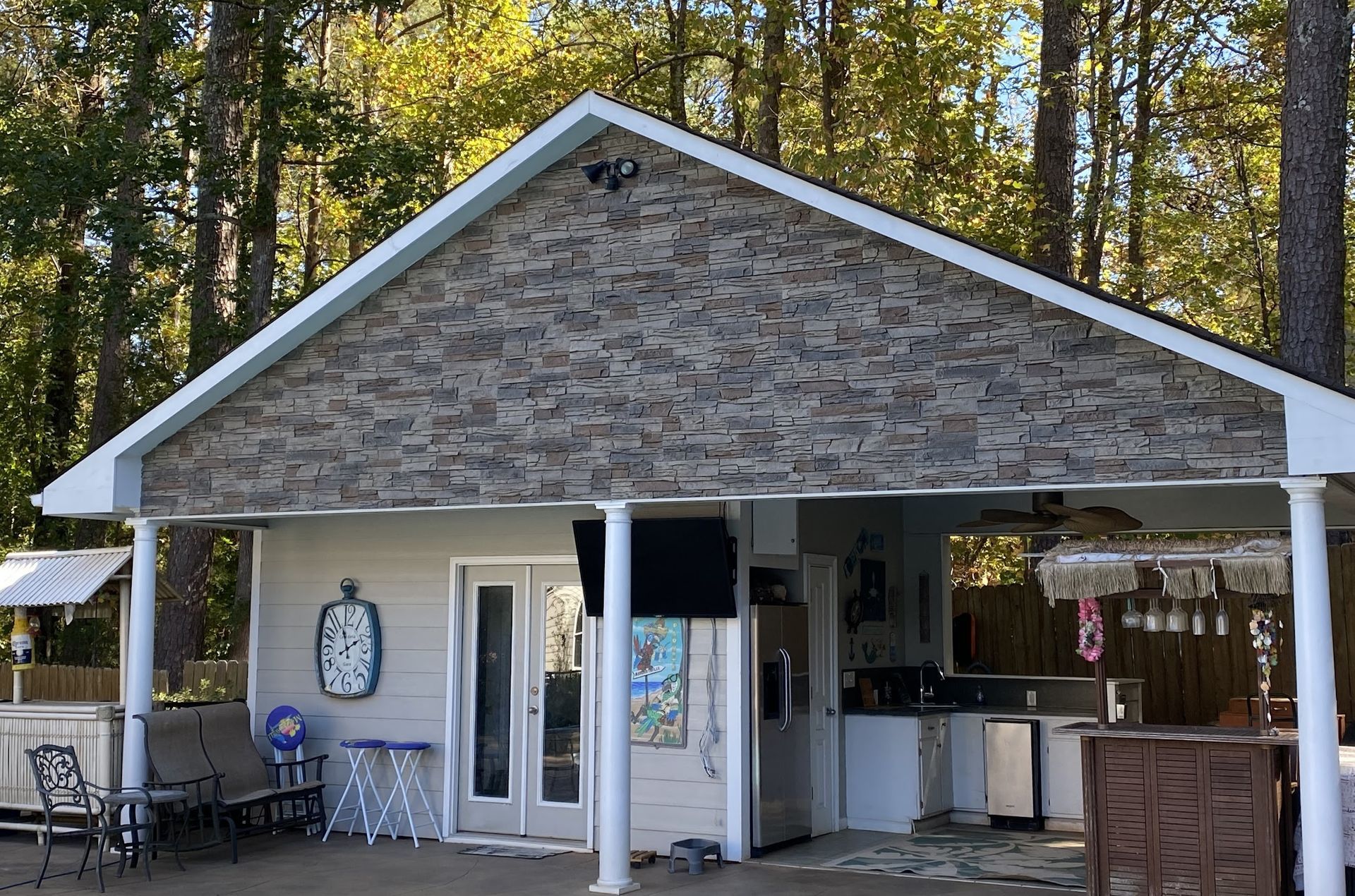 A white house with a stone roof and a porch surrounded by trees.