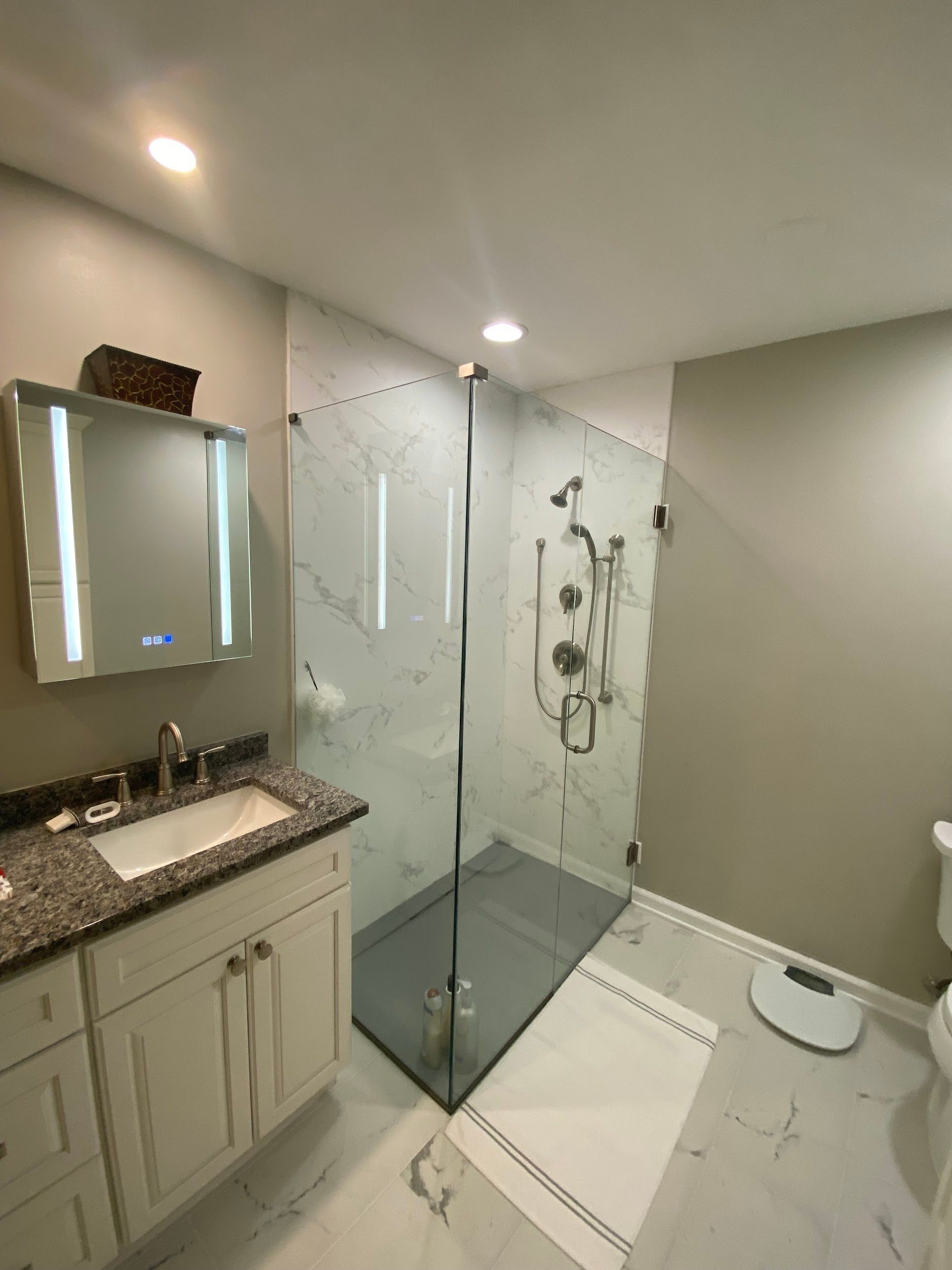 A bathroom with a walk in shower , sink , mirror and scale.
