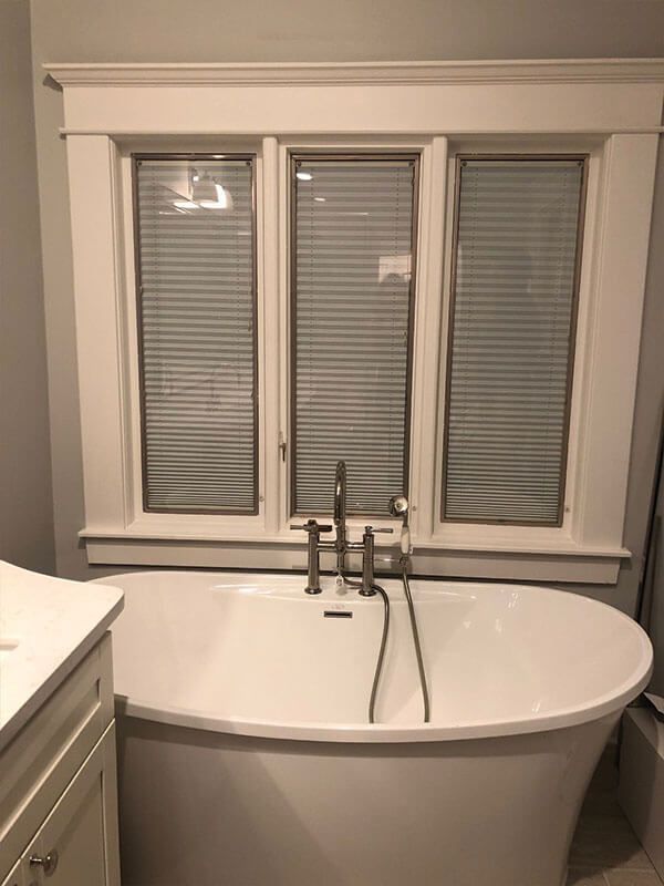 A bathtub in a bathroom next to a window with blinds.