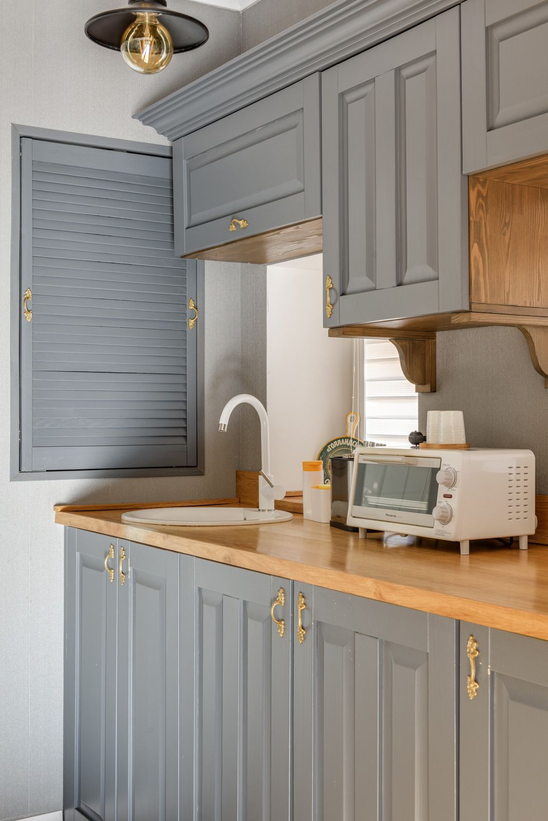 A kitchen with gray cabinets , a sink , a microwave , and a window.