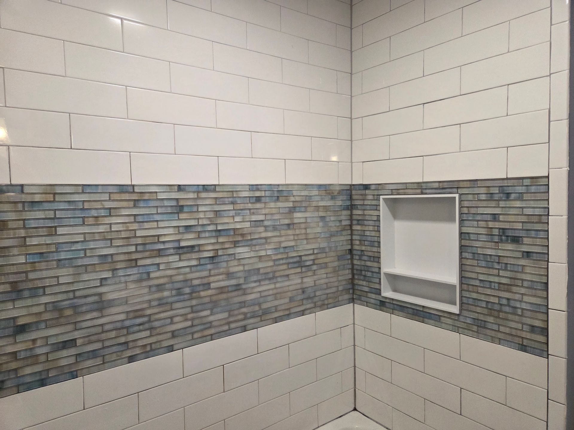 A bathroom with white tiles and a shelf in the corner.