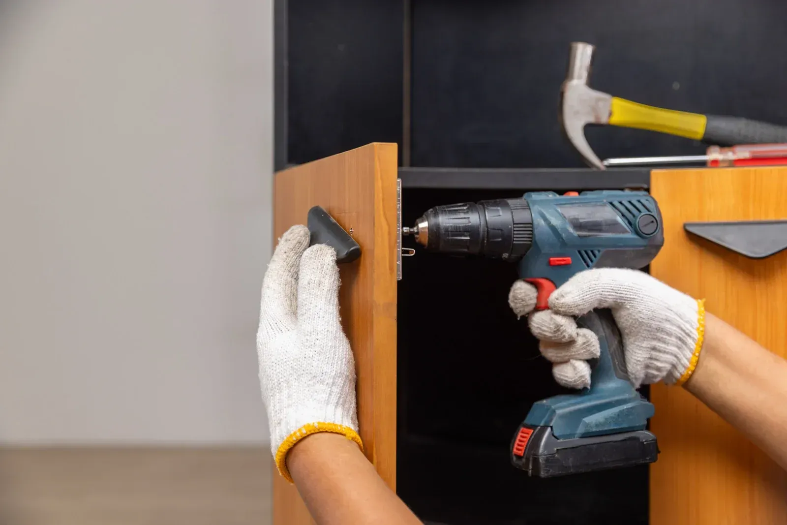 Hands holding a tablet, surrounded by architectural plans, color swatches, and a laptop on a white surface.