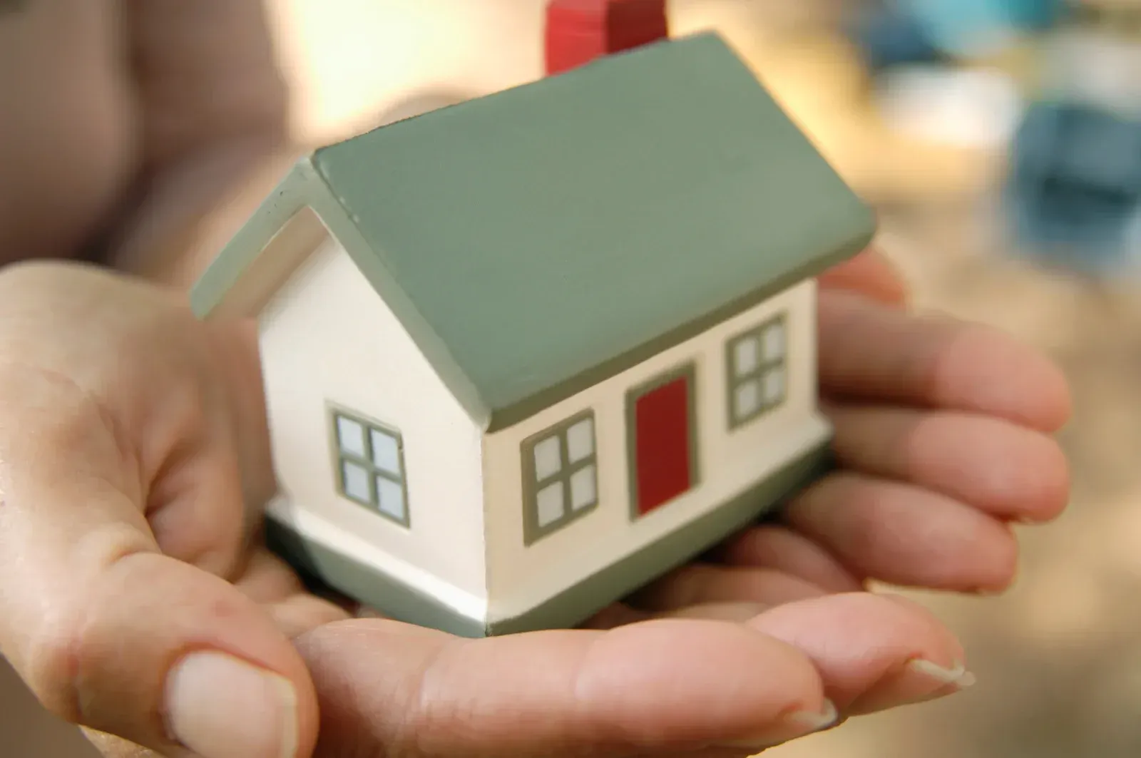 A person is holding a small model house in their hands.