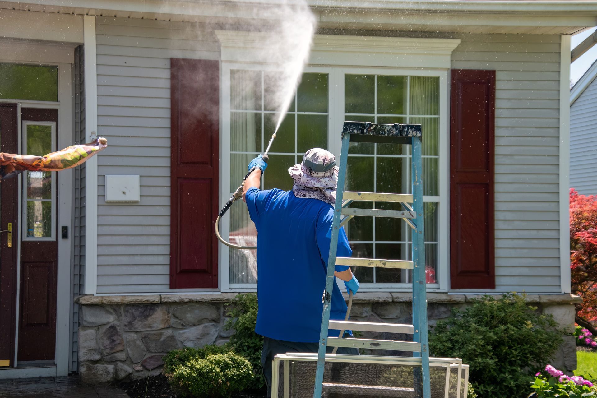 a man on a ladder cleaning a house with a high pressure washer