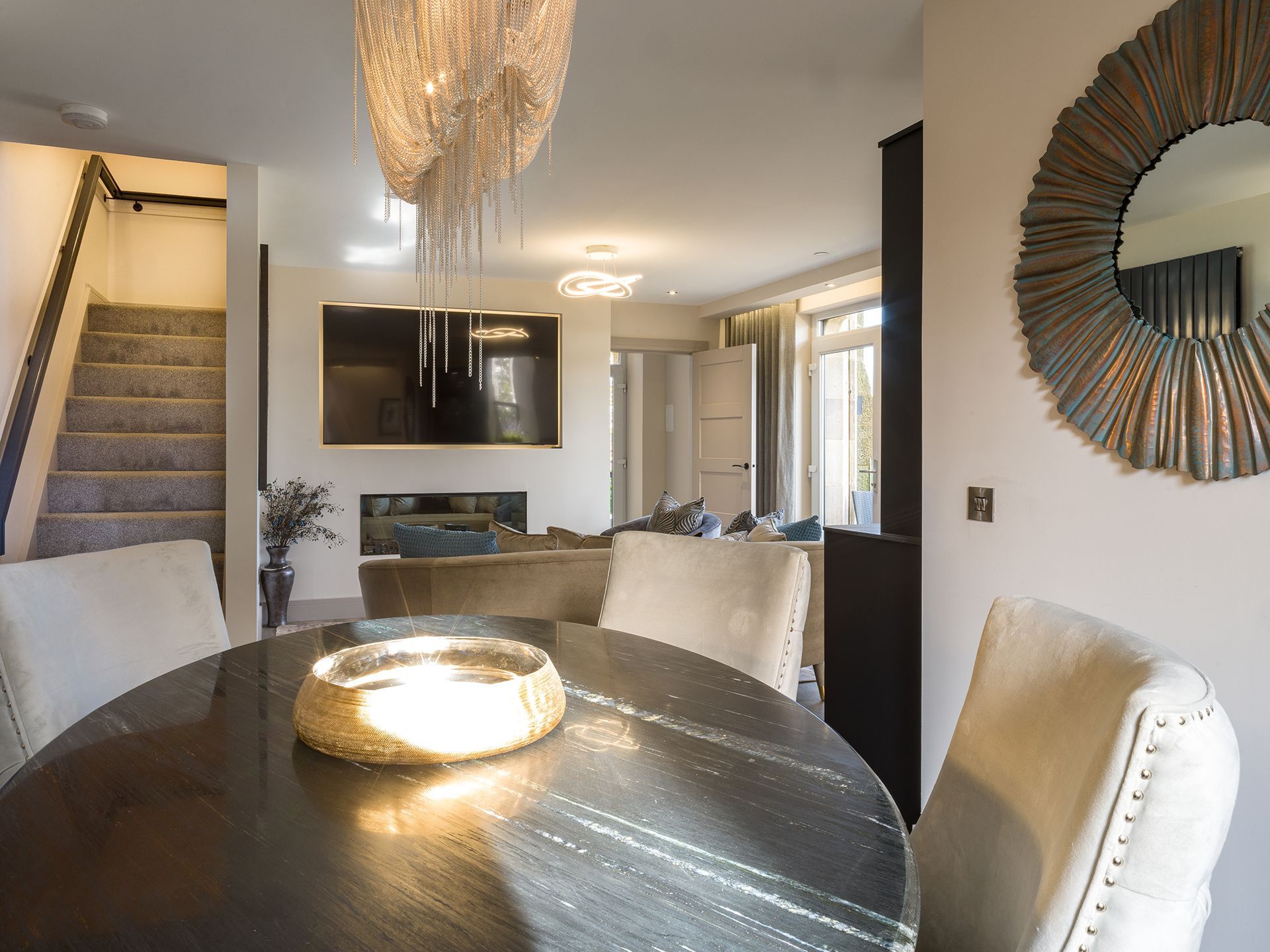 A dining room with a round table and chairs and a mirror on the wall.