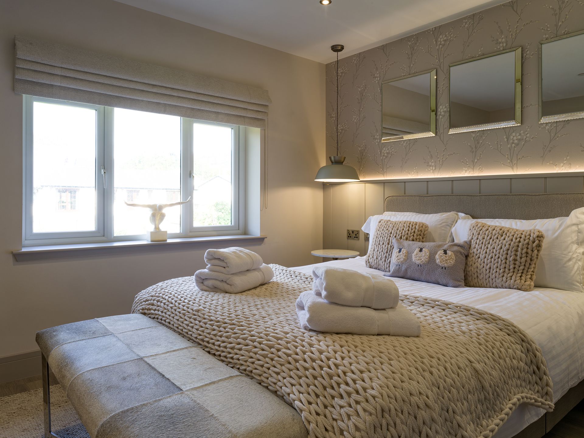 A bedroom with a bed , window , bench and mirrors.