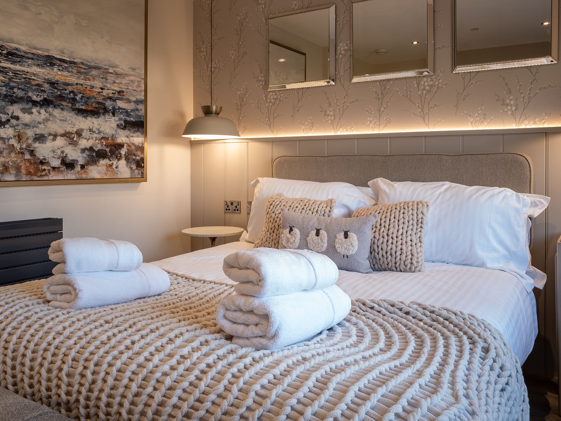 A bedroom with a bed , pillows , towels and a painting on the wall.