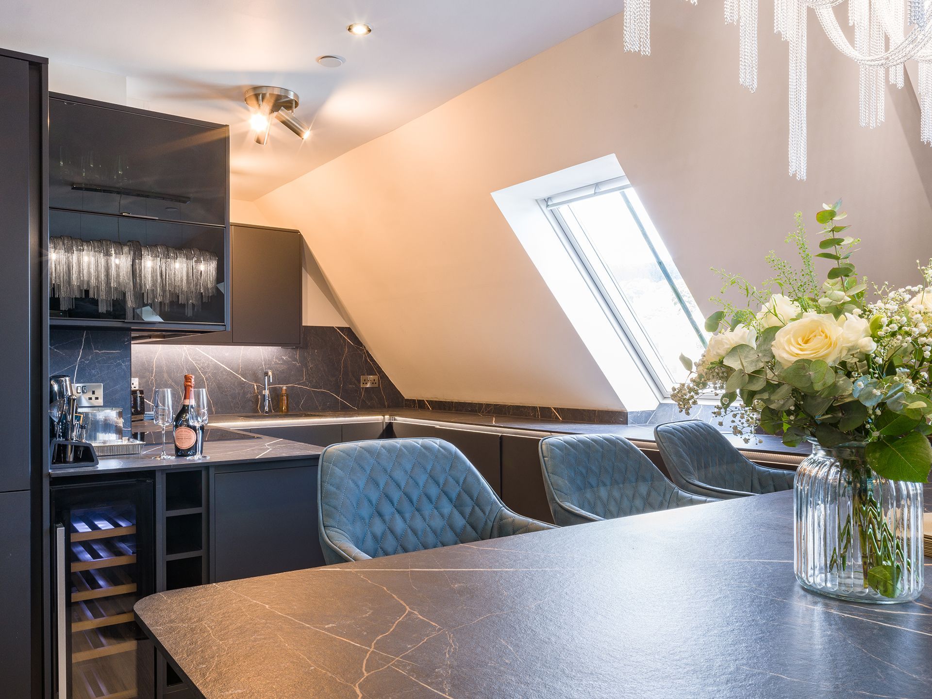 A kitchen with a table and chairs and a vase of flowers on the table.