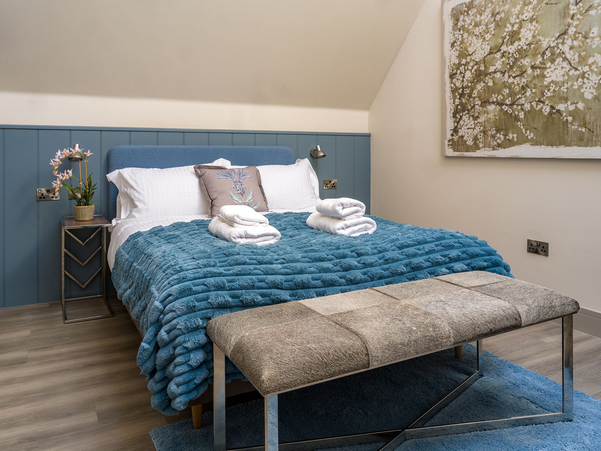 A bedroom with a bed , bench , nightstand and painting on the wall.