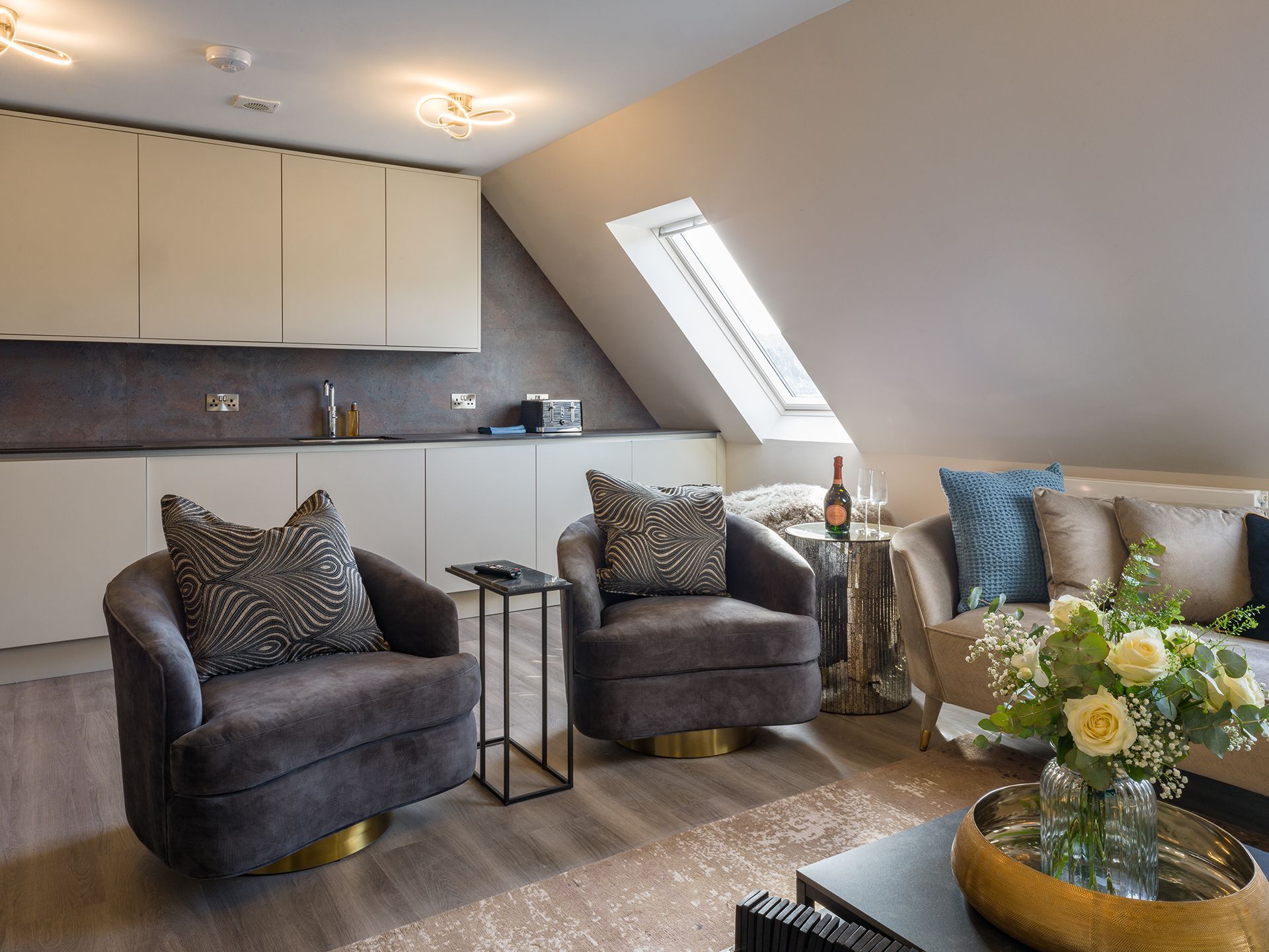 A living room with a couch , two chairs , a coffee table and a vase of flowers.