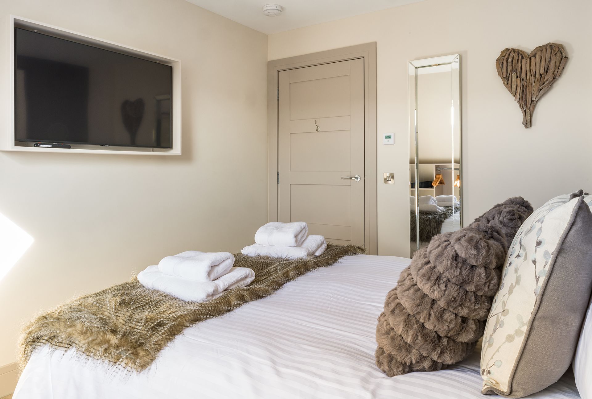 A bedroom with a bed , television , mirror and heart on the wall.