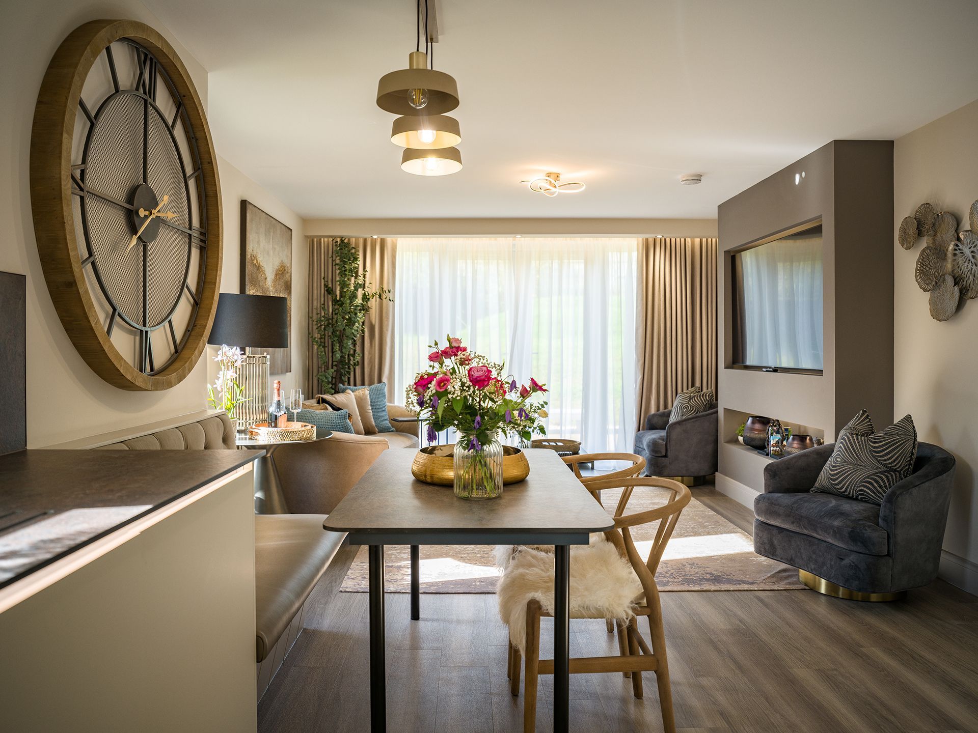 A living room with a table and chairs and a large clock on the wall.