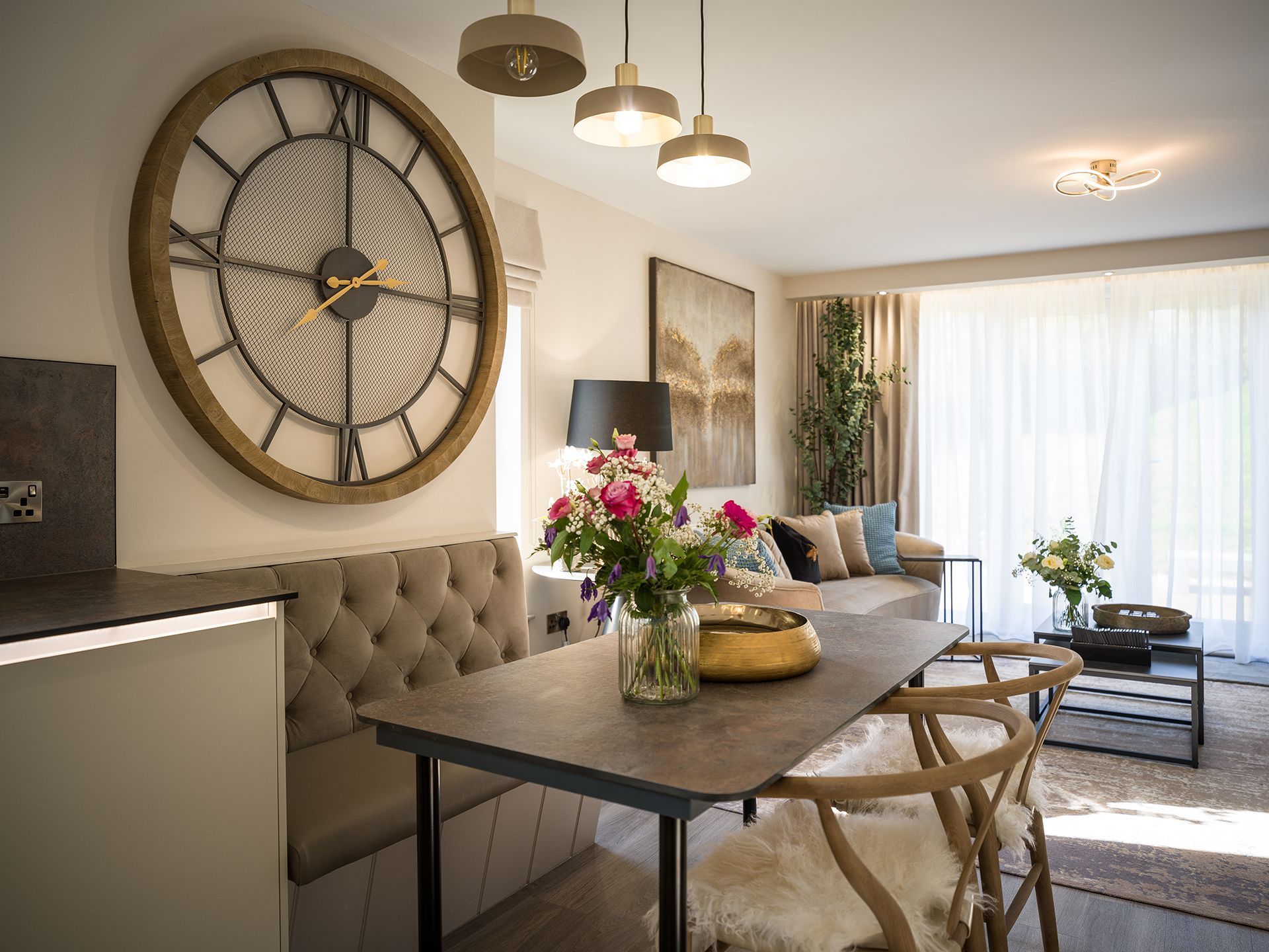 A living room with a table and chairs and a large clock on the wall.