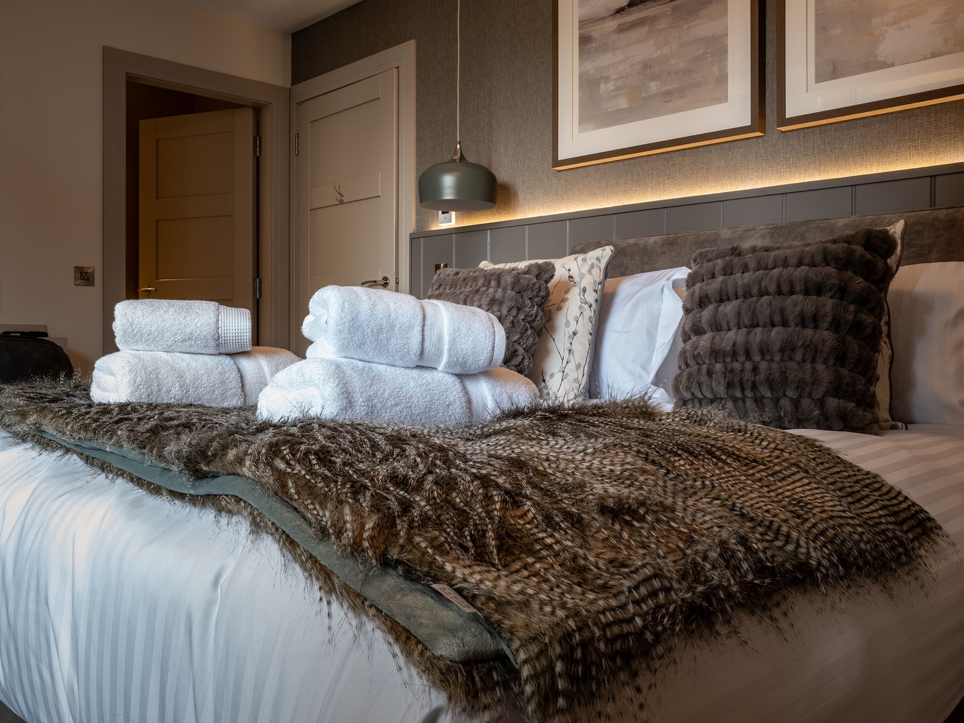 A bed with a fur blanket and towels on it in a bedroom.