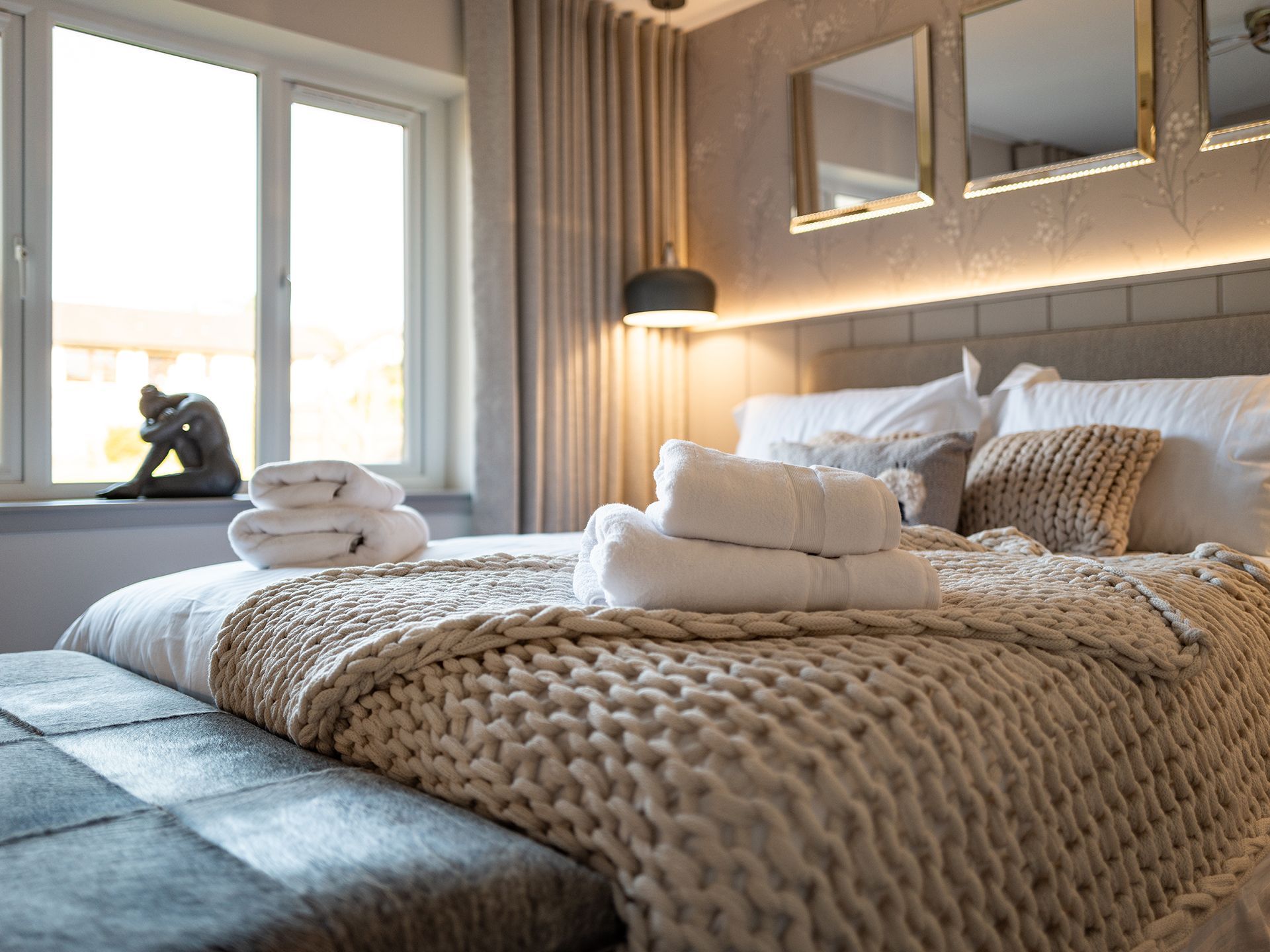 A bedroom with a bed , two mirrors , and a window.