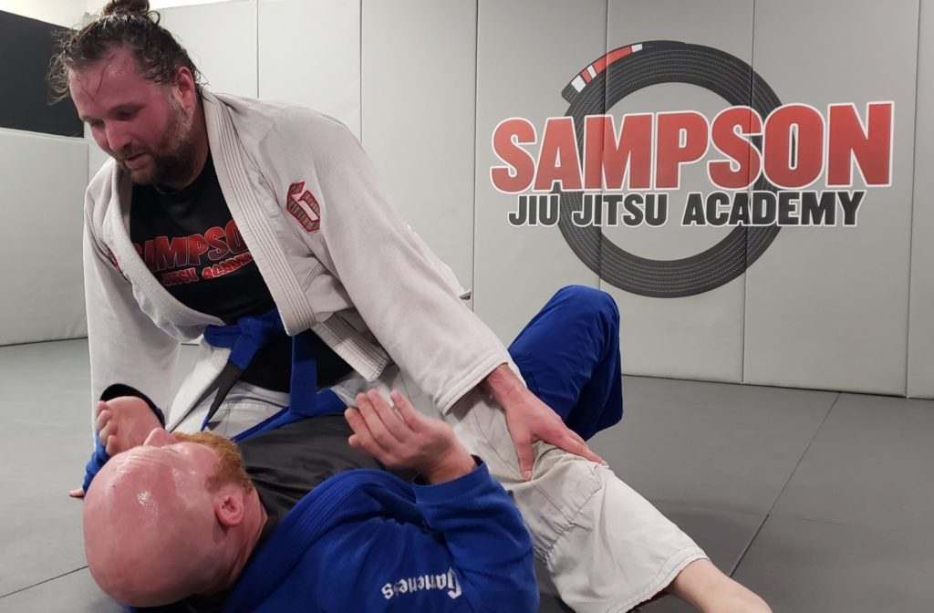 Two men are wrestling in a gym with sampson jiu jitsu academy in the background.