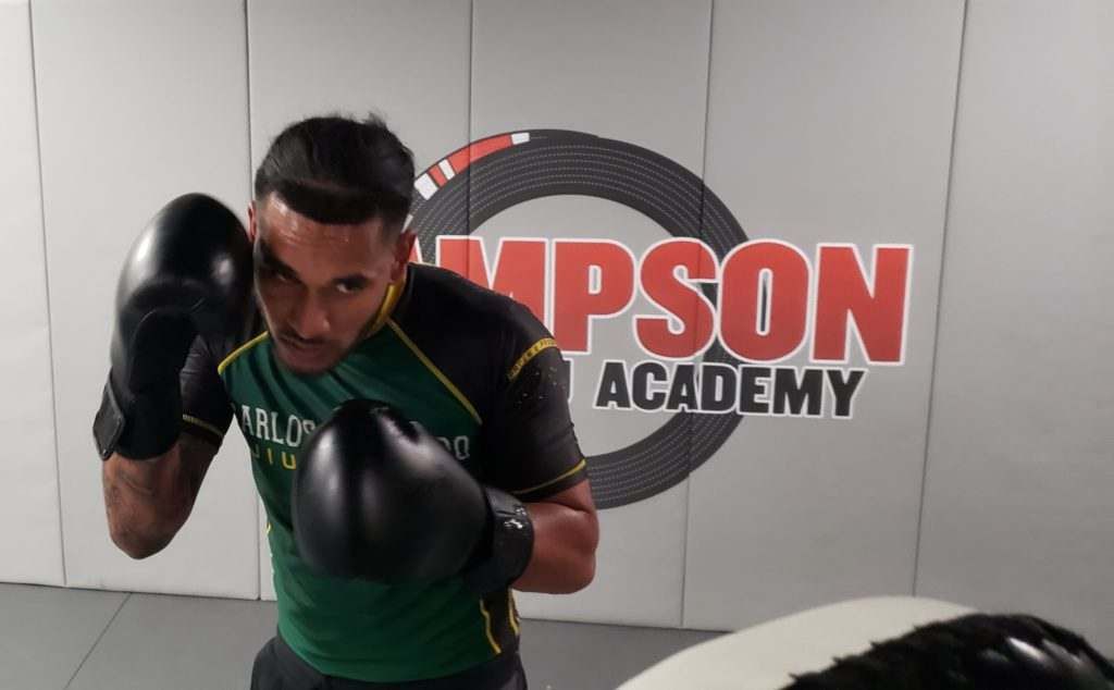 A man wearing boxing gloves in front of a wall that says ' simpson academy '