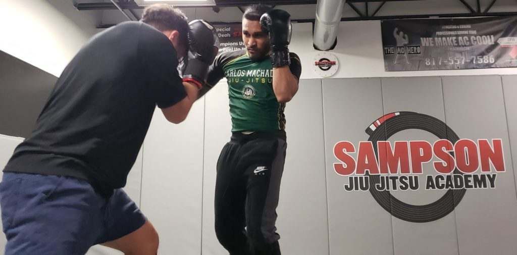 Two men are boxing in a gym with a sign that says sampson jiu jitsu academy.