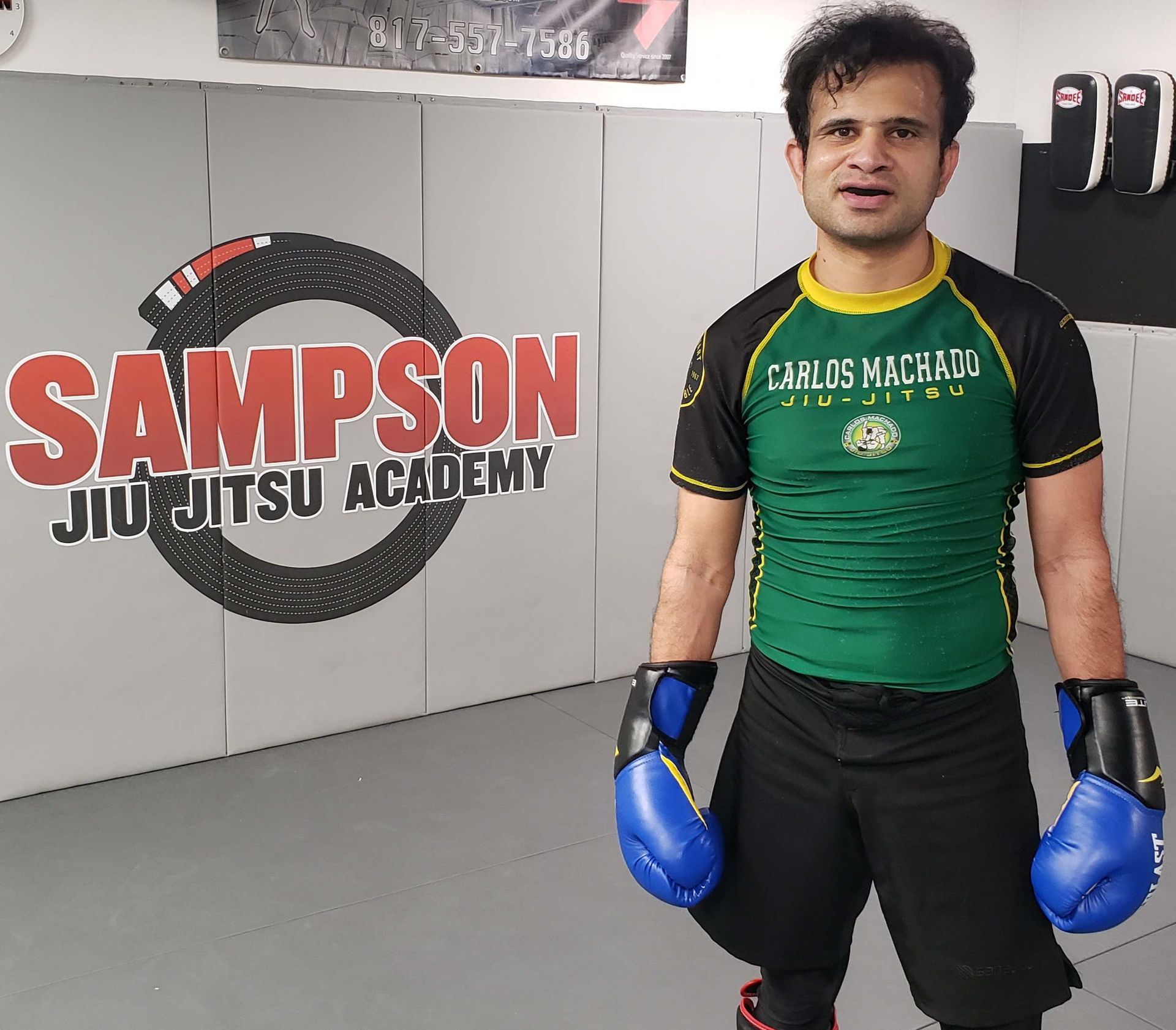 A man is standing in front of a wall that says sampson jiu jitsu academy