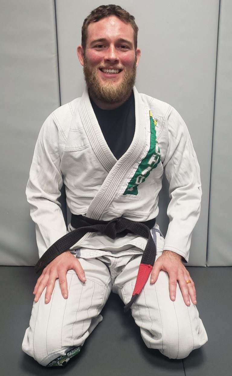 A man in a karate uniform is kneeling down and smiling.