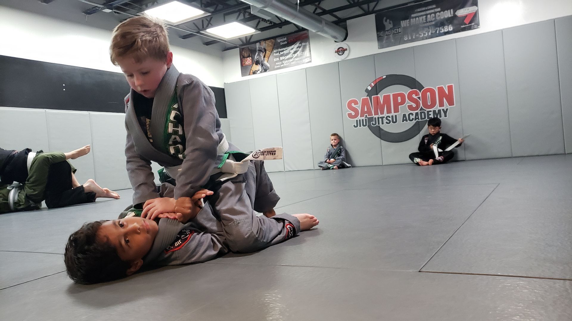 Two young boys are practicing jiu jitsu in a gym.