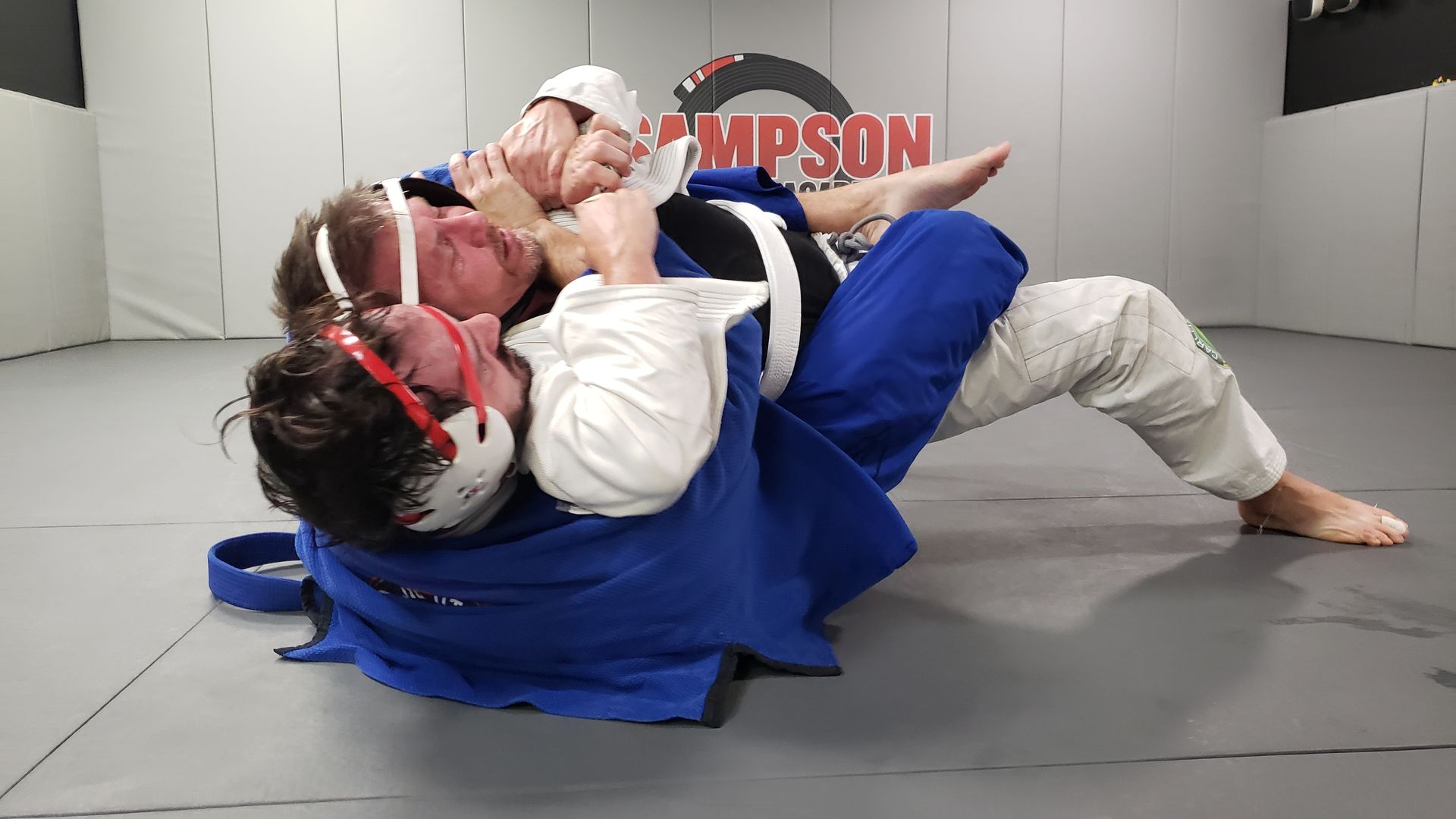 Two men are wrestling in a gym with the word simpson on the wall.
