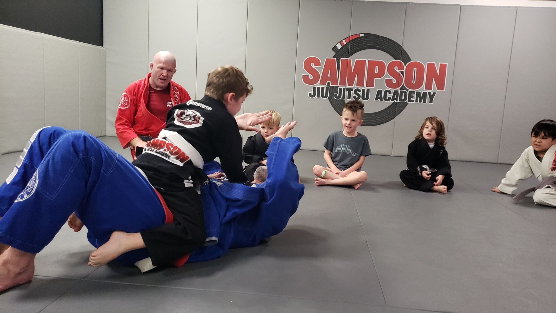 A group of children are practicing jiu jitsu in a gym.