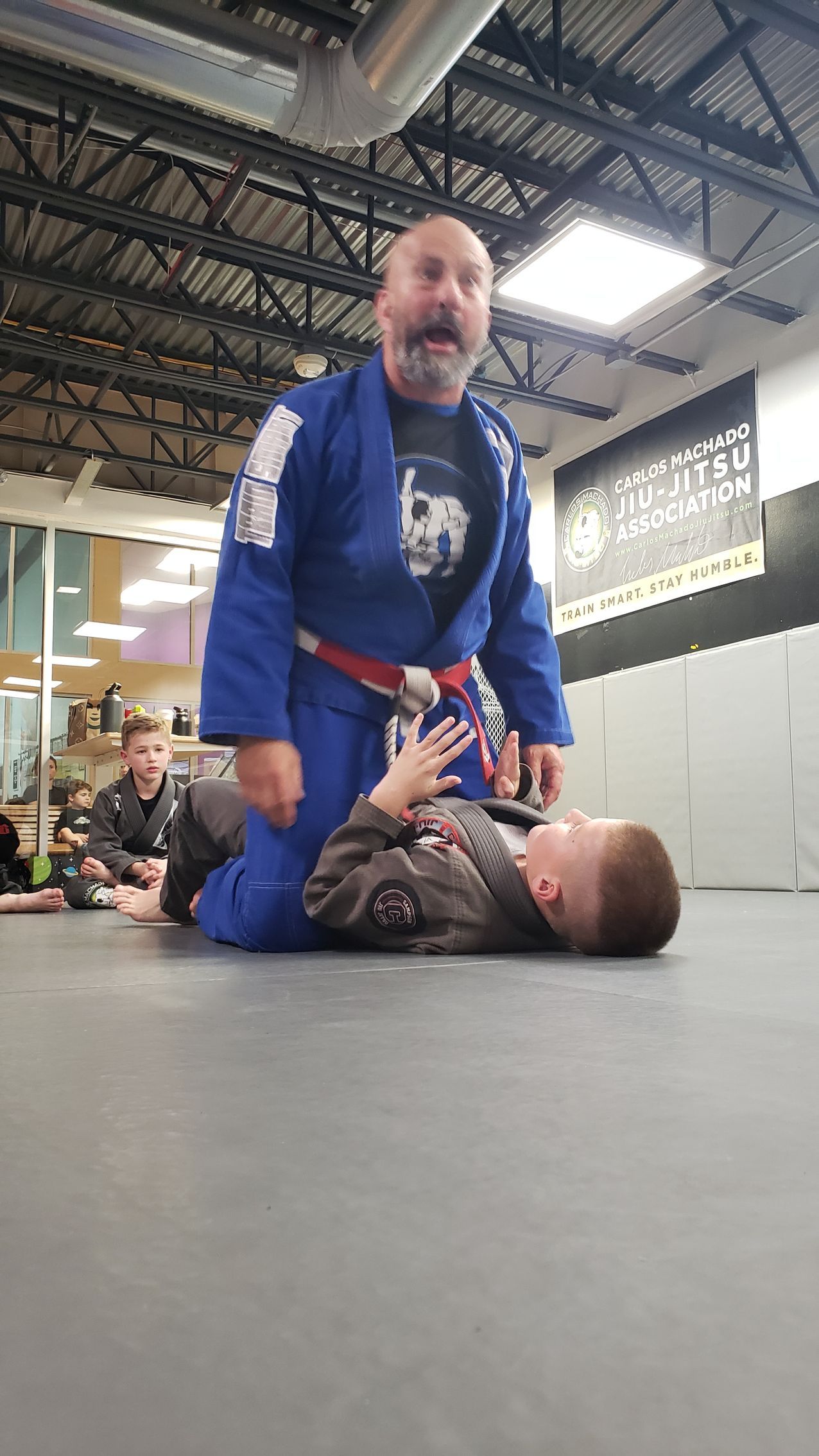 A man in a blue kimono is teaching a young boy how to do a karate move.
