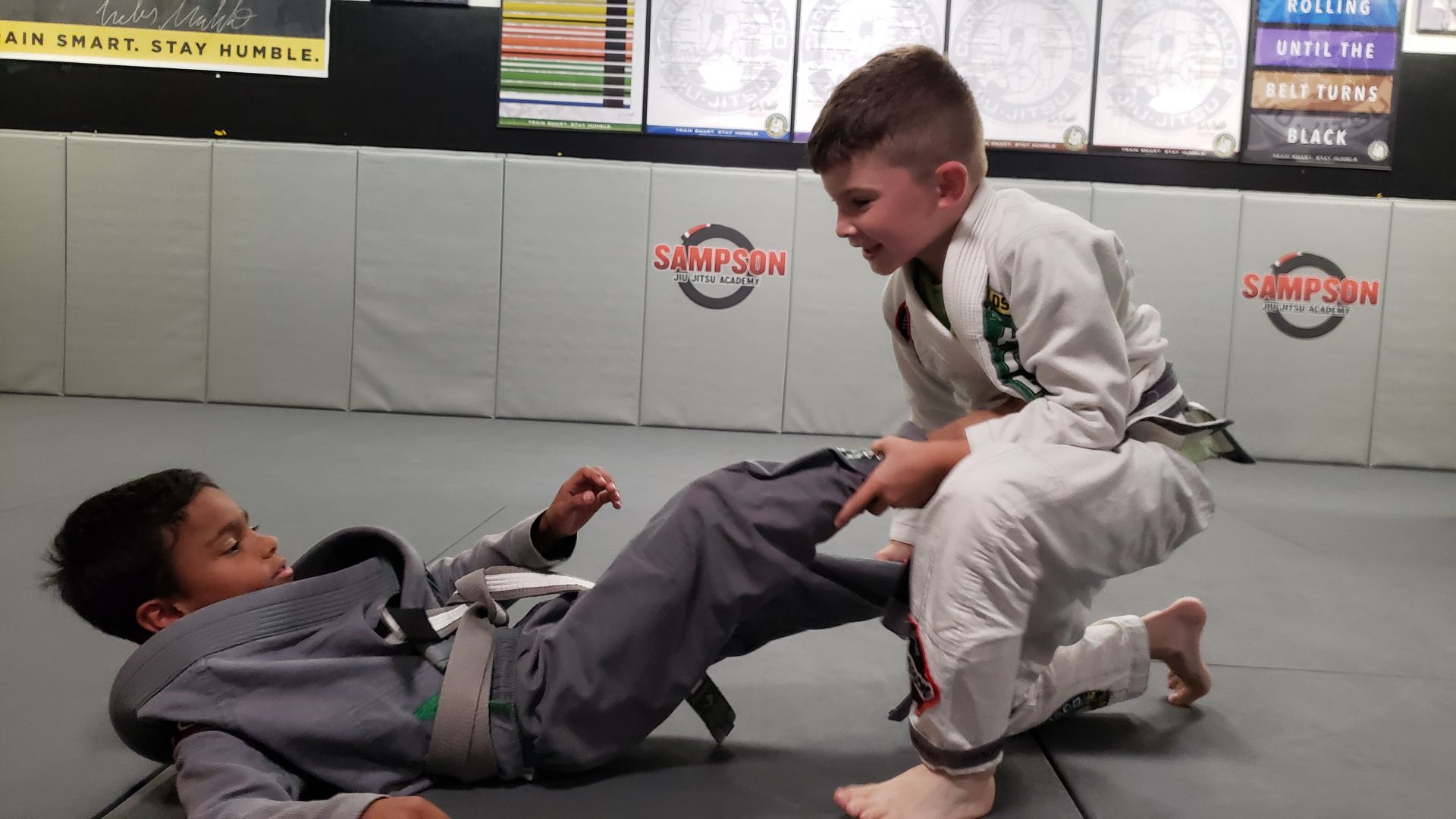 Two young boys are practicing jiu jitsu in a gym.