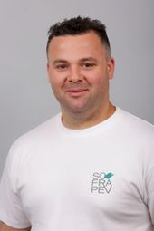 Un homme porte un t-shirt blanc et sourit à la caméra.