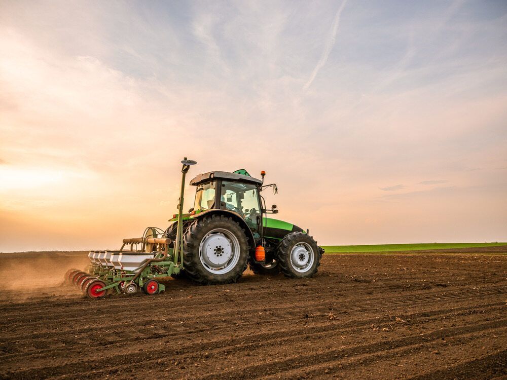 A Green Tractor is Plowing a Field at Sunset — Coffs Harbour Bearing Centre in Coffs Harbour, NSW