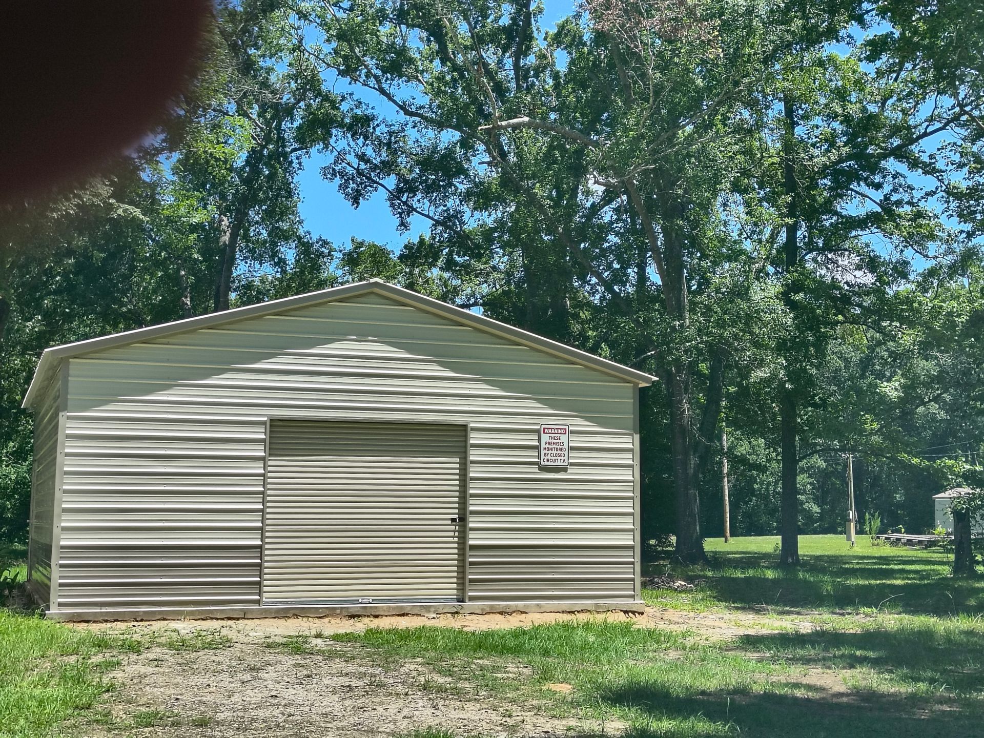 Light beige metal shed with a closed sliding door, surrounded by trees and grass on a sunny day.