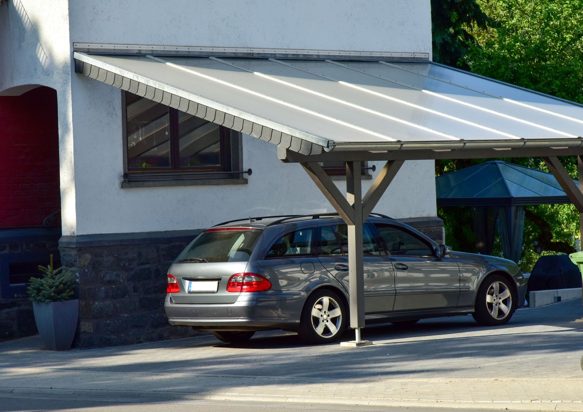 Car parked under a carport attached to a building, light grey roof, grey car.