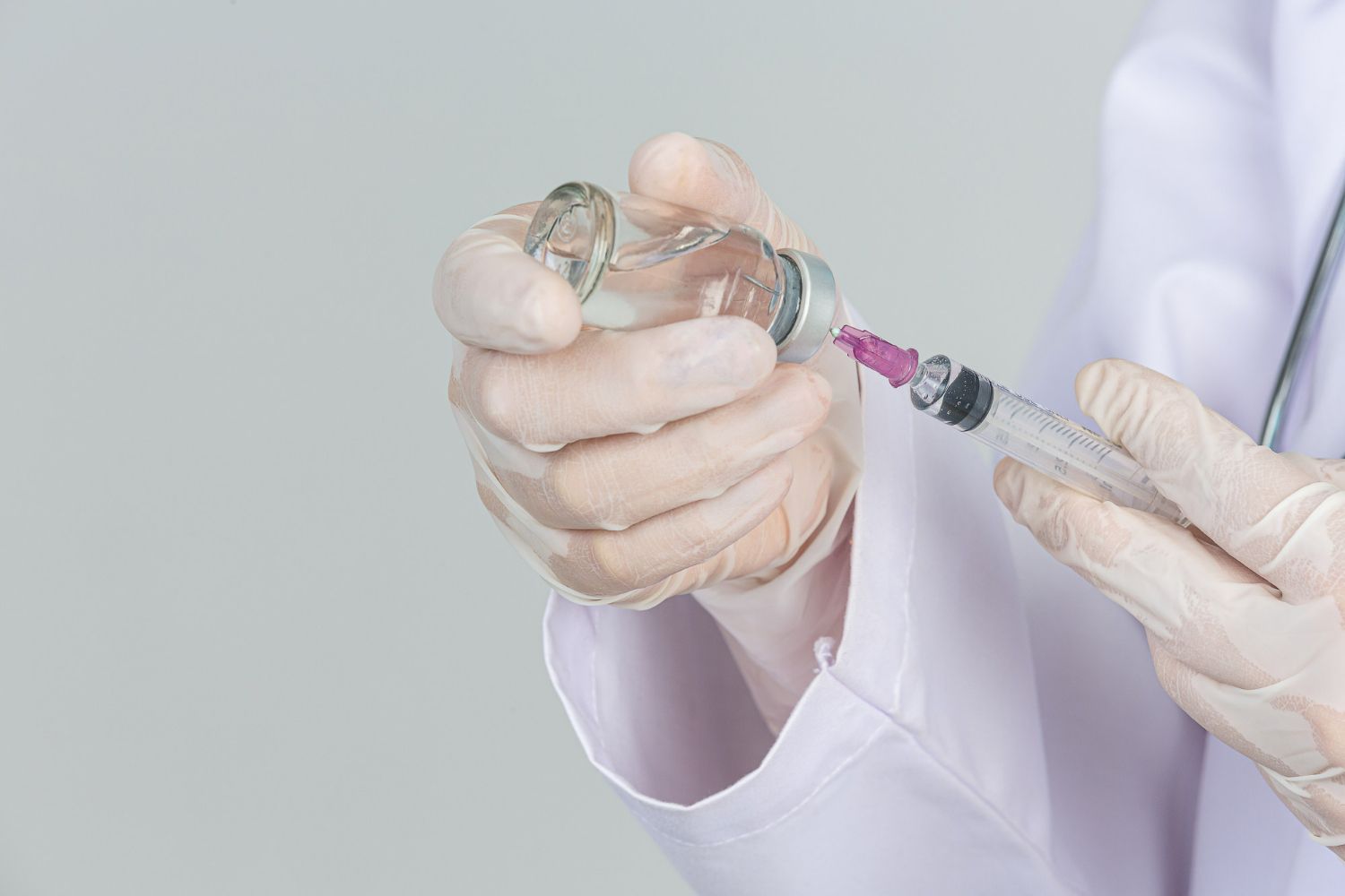 Person in gloves filling a syringe from a medicine vial, likely for an injection.