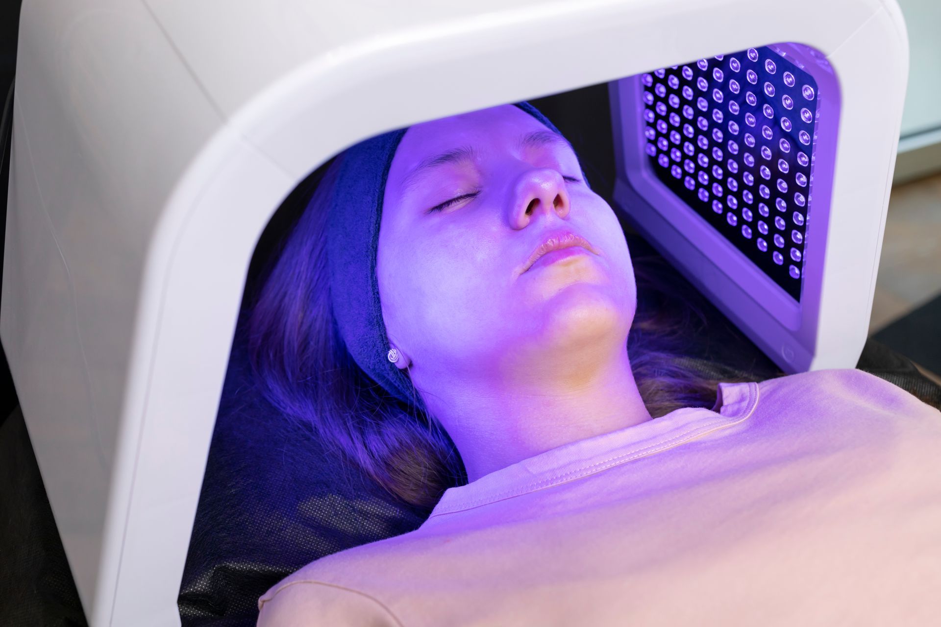 A woman is laying in a chair with a purple light on her face.