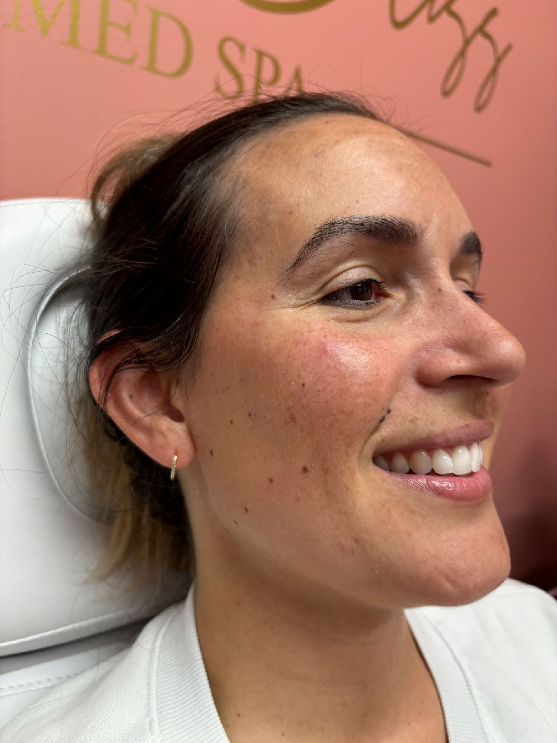 A woman is smiling while sitting in a chair in front of a pink wall.