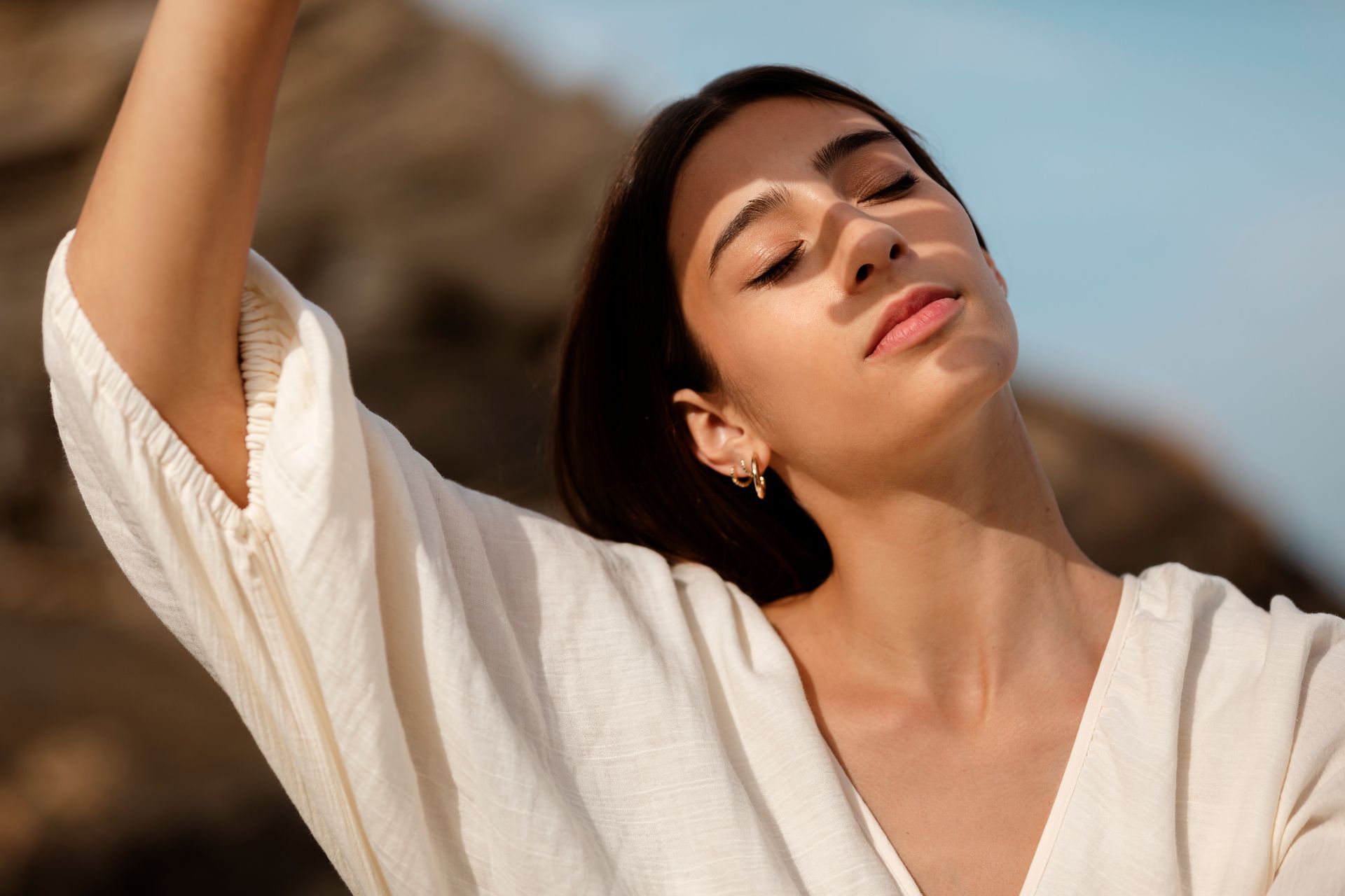 A woman in a white shirt is standing on a beach with her arms outstretched.