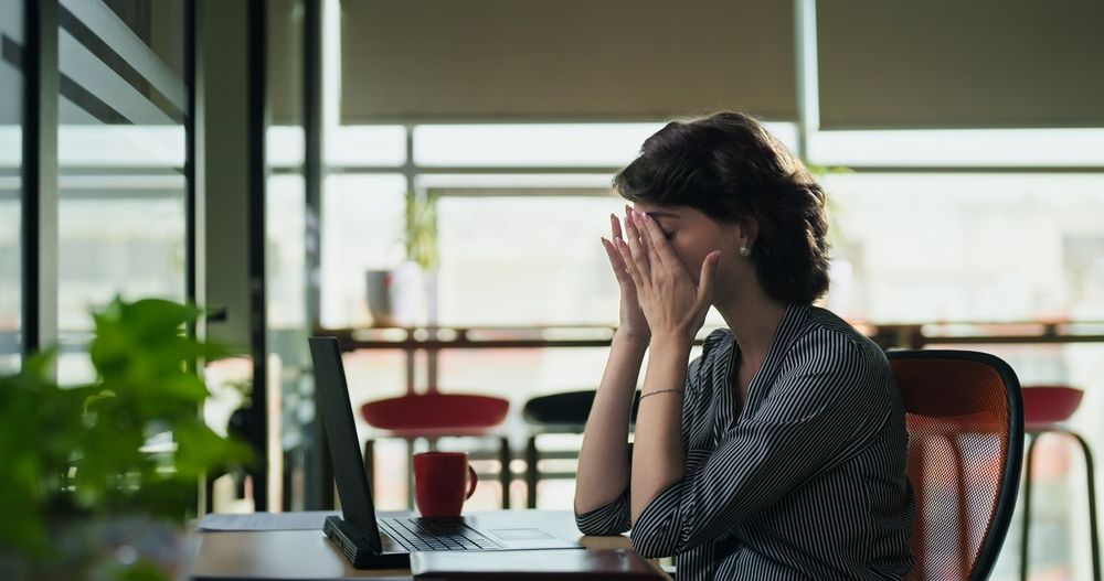 A woman is sitting at a desk with her hands on her face.