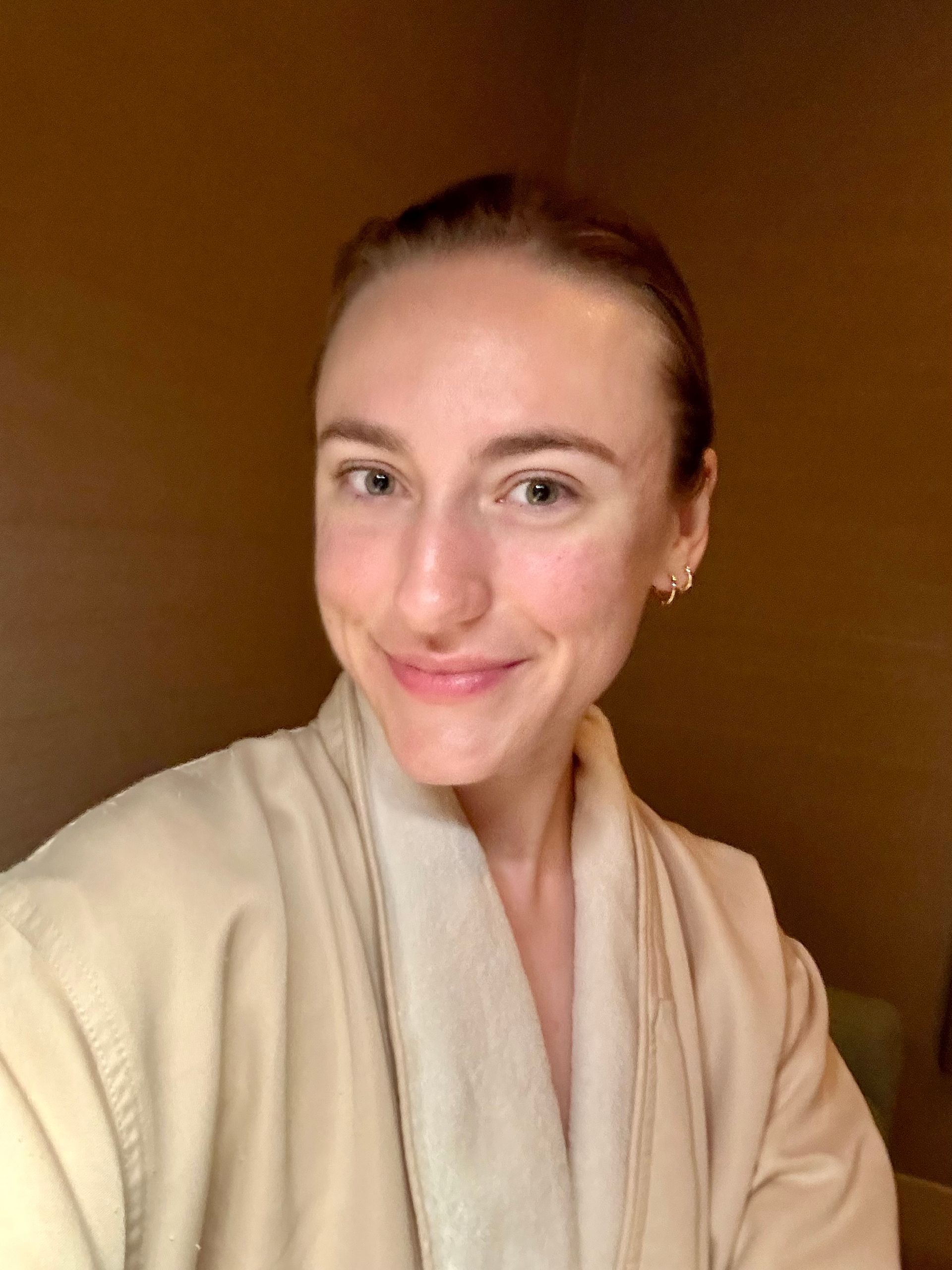 A woman in a bathrobe is smiling and taking a selfie.