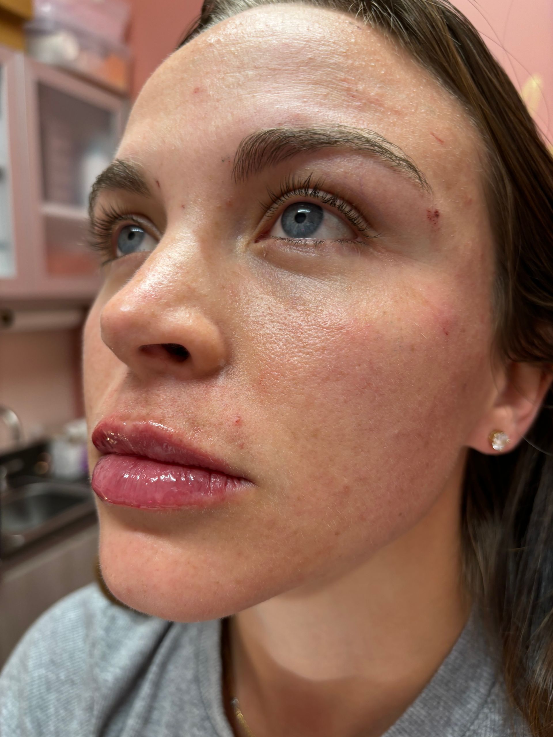 A close up of a woman 's face with a pink lip gloss on her lips.