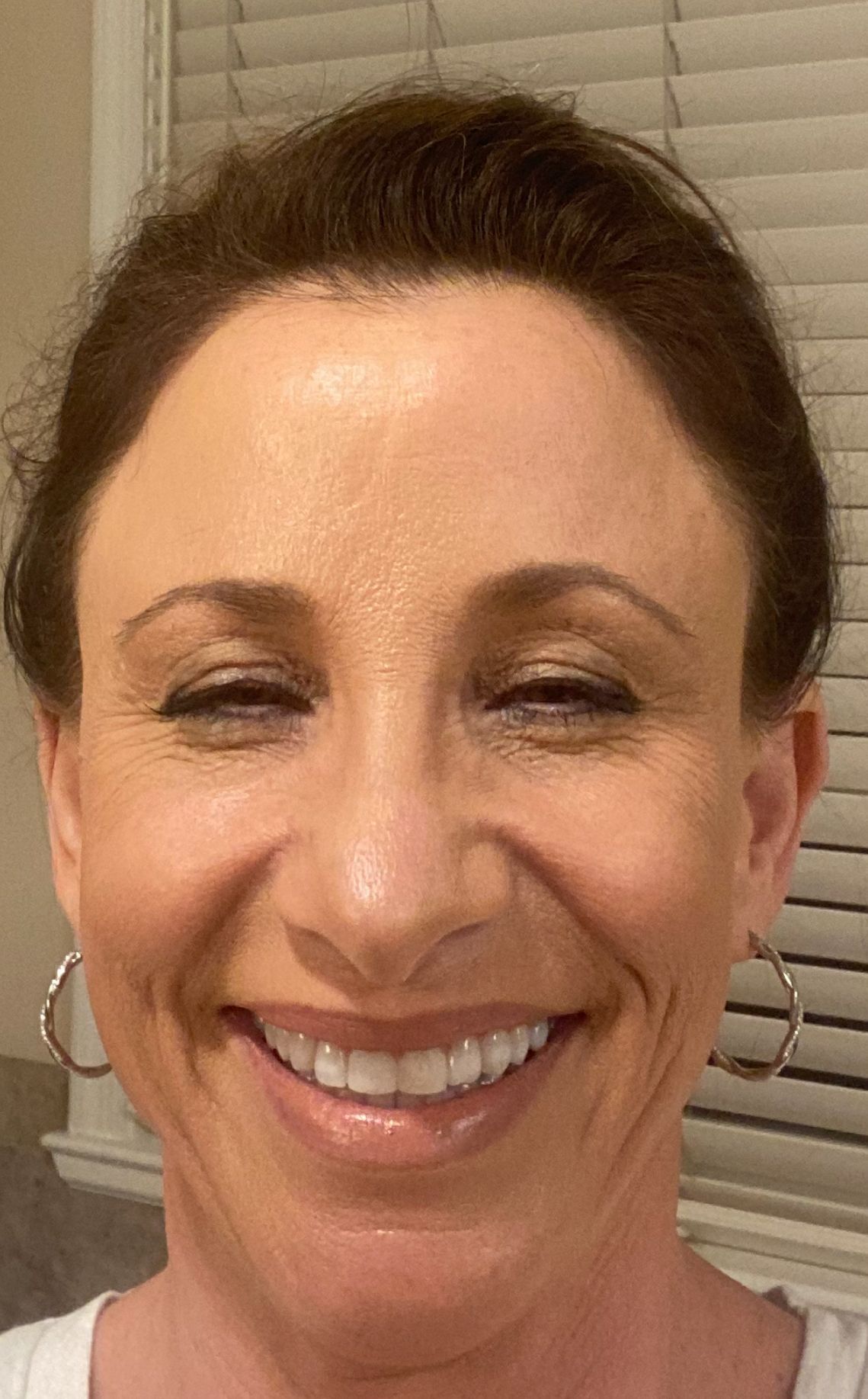 A close up of a woman 's face smiling in front of a window.