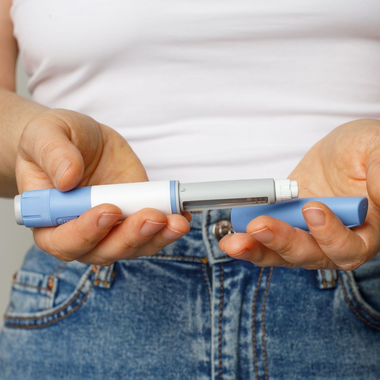 A woman is holding a blue and white insulin pen in her hands.