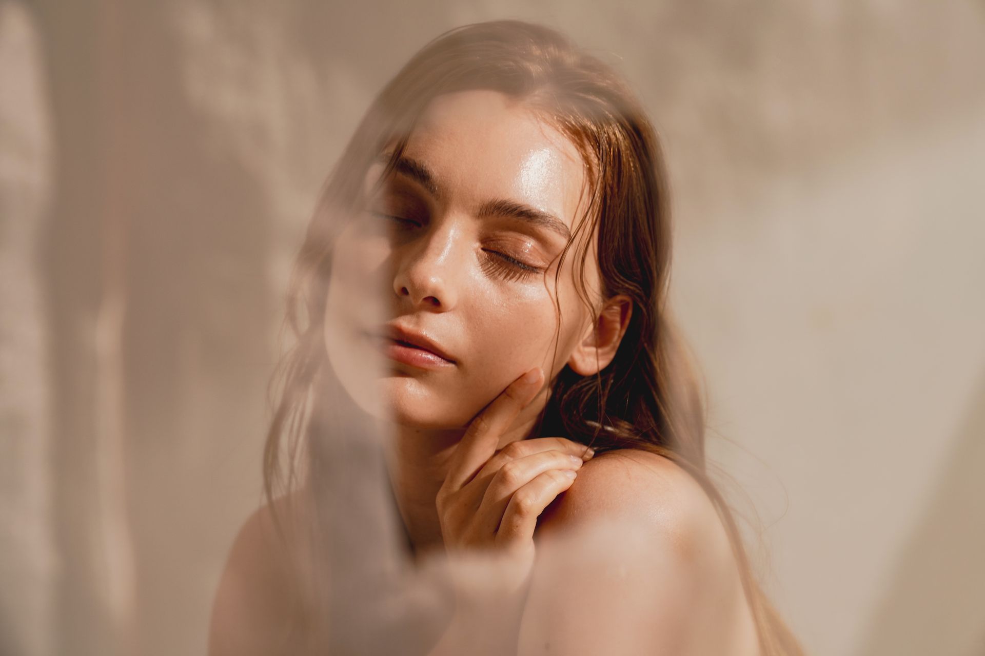Woman with closed eyes, gently touching her face, bathed in soft light.