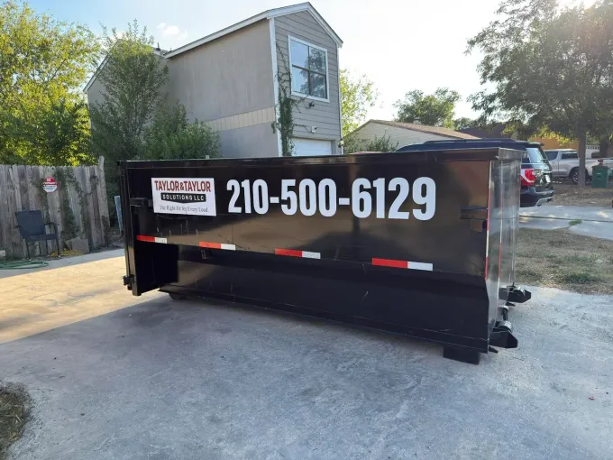 A dumpster is parked in front of a brick house
