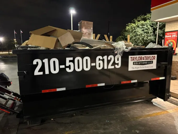 A dumpster is sitting on the side of the road in front of a city skyline.