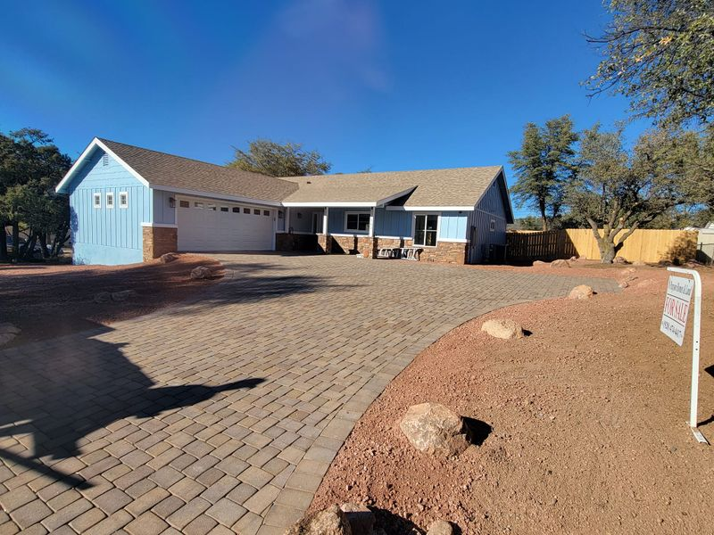 Suburban house with blue garage, paver driveway, and desert landscaping under a clear sky