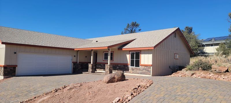 Single-story beige house with a garage, desert landscaping, and a stone driveway under a clear blue sky