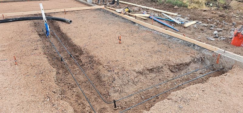 Construction site with a muddy rectangular foundation area and scattered tools along the edges