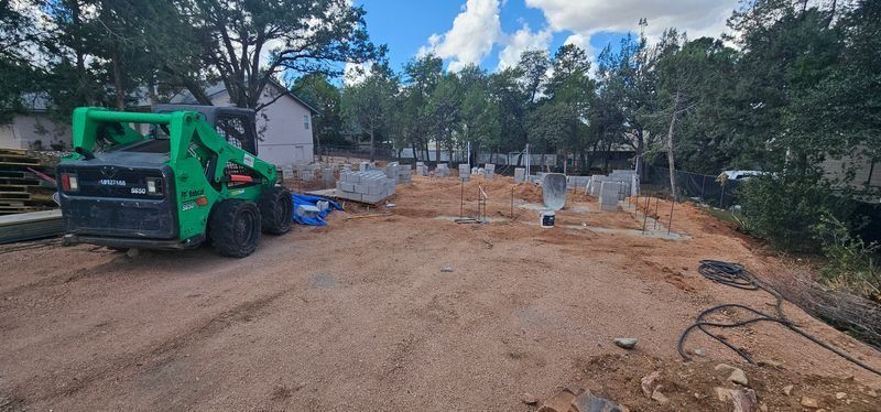 Green construction vehicle on a dirt road beside excavated ground and trees under a cloudy sky