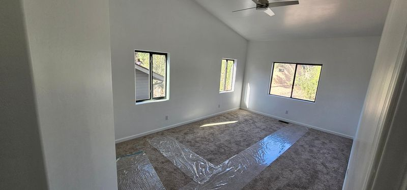 Empty unfurnished bedroom with white walls, carpet, and three windows letting in daylight